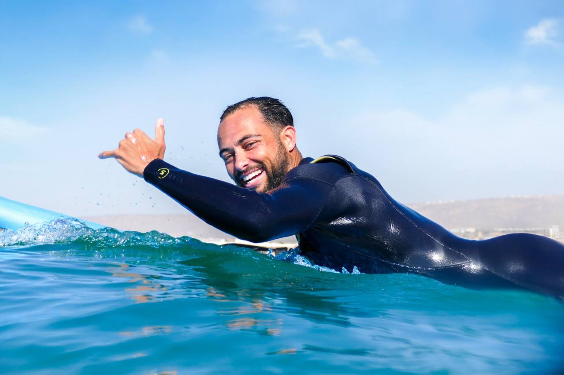 Surf coach giving shaka sign in the water at Taghazout