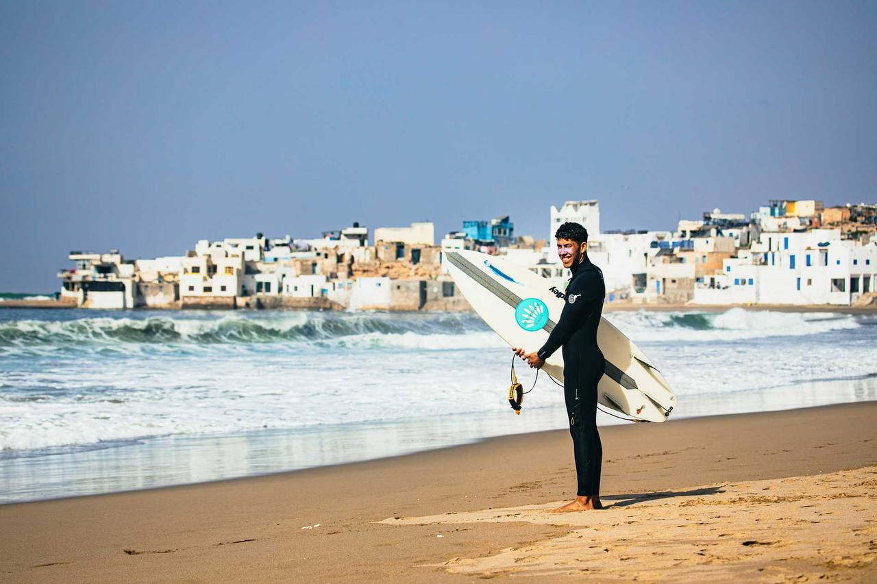 Surfer on the beach with Taghazout coastline in the background